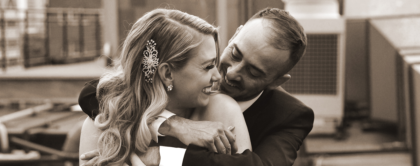 A bride wearing a dazzling barrette in her hair and being embraced by her husband